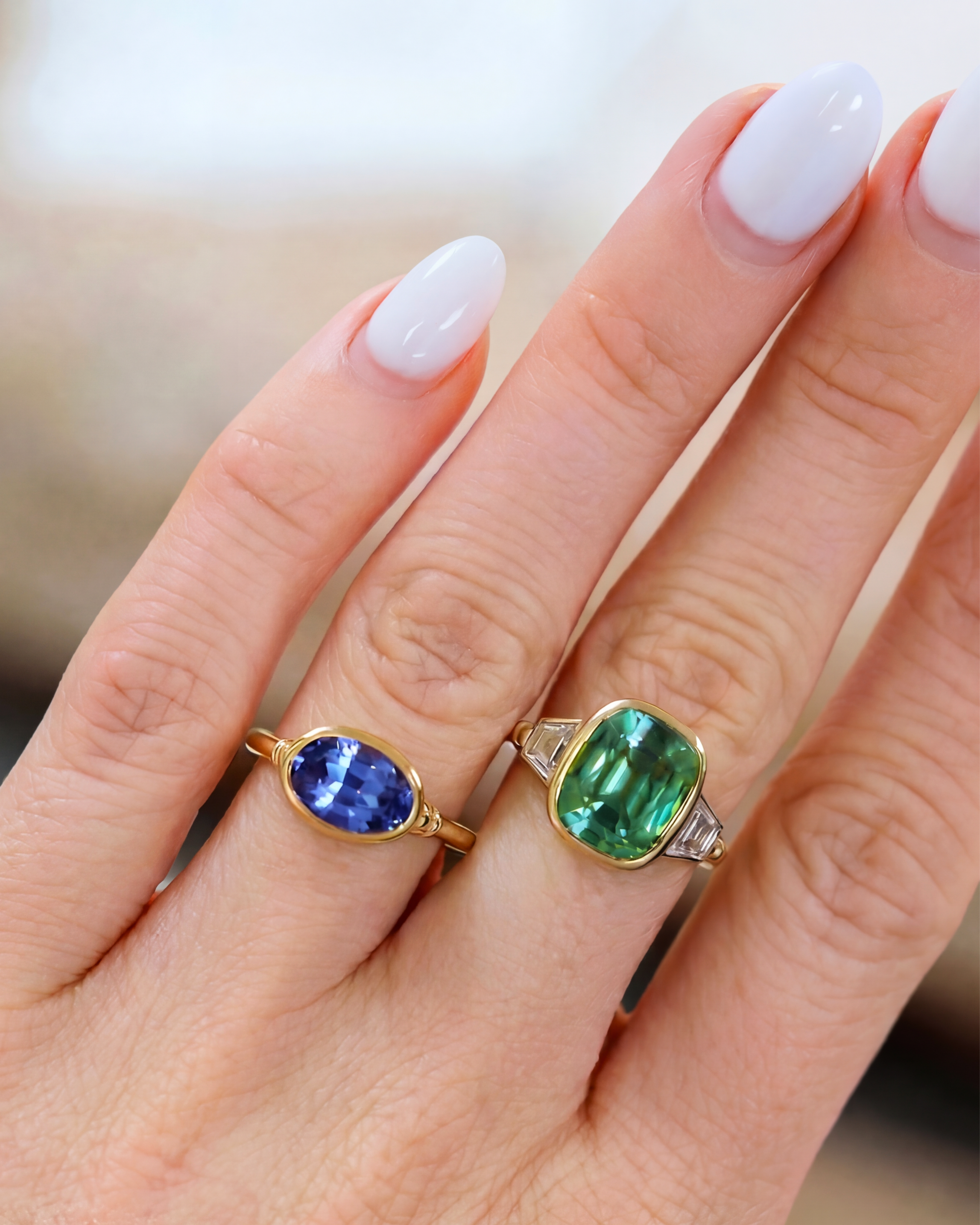 Two rings with gemstones on a hand against a blurred background