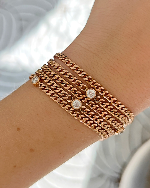 Rose gold chain bracelet with diamond-like stones on a wrist against a neutral background