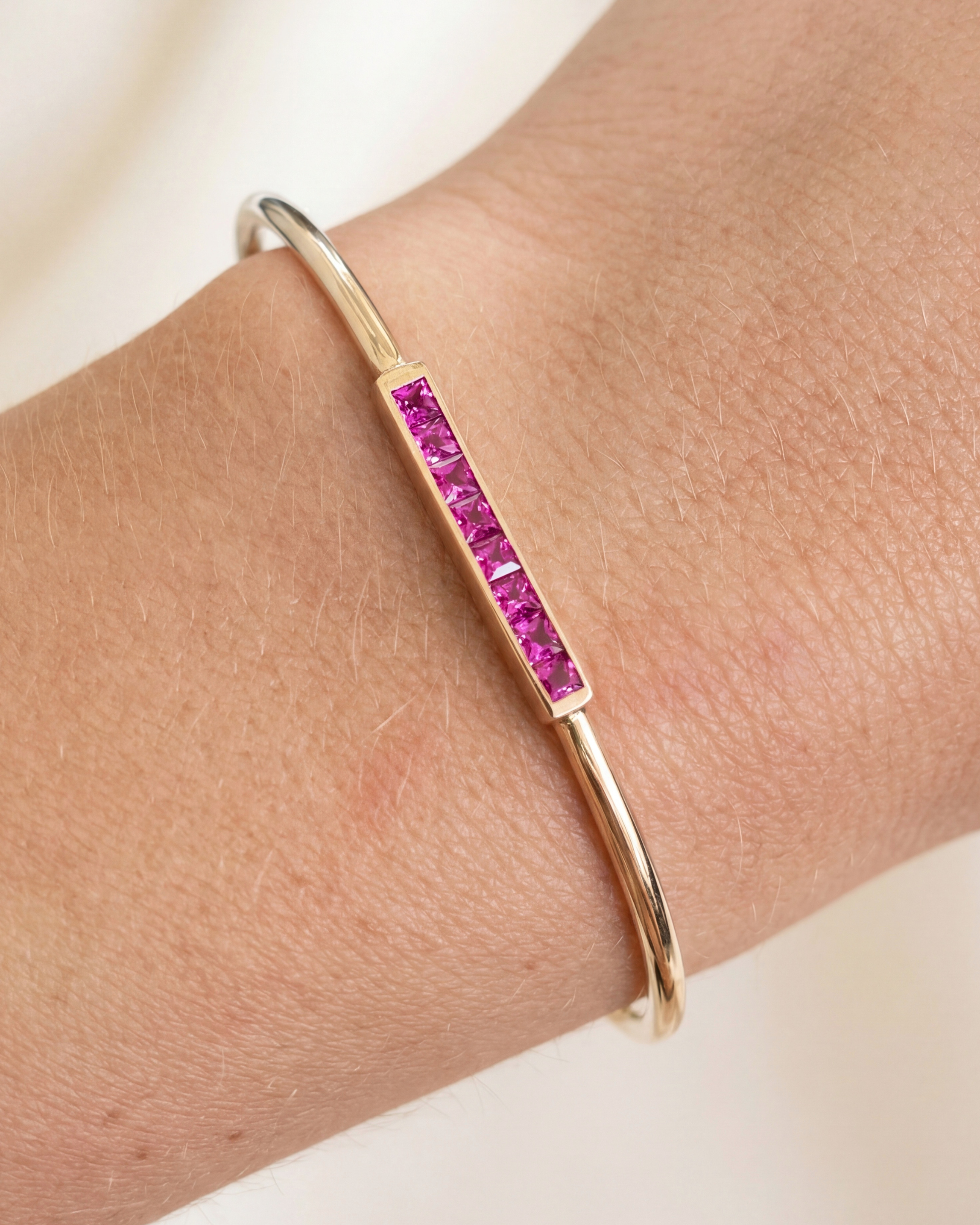 Gold bracelet with pink gemstones on a wrist against a neutral background