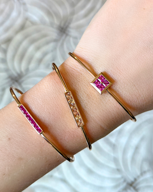 Gold bracelets with pink gemstones on a wrist against a neutral background