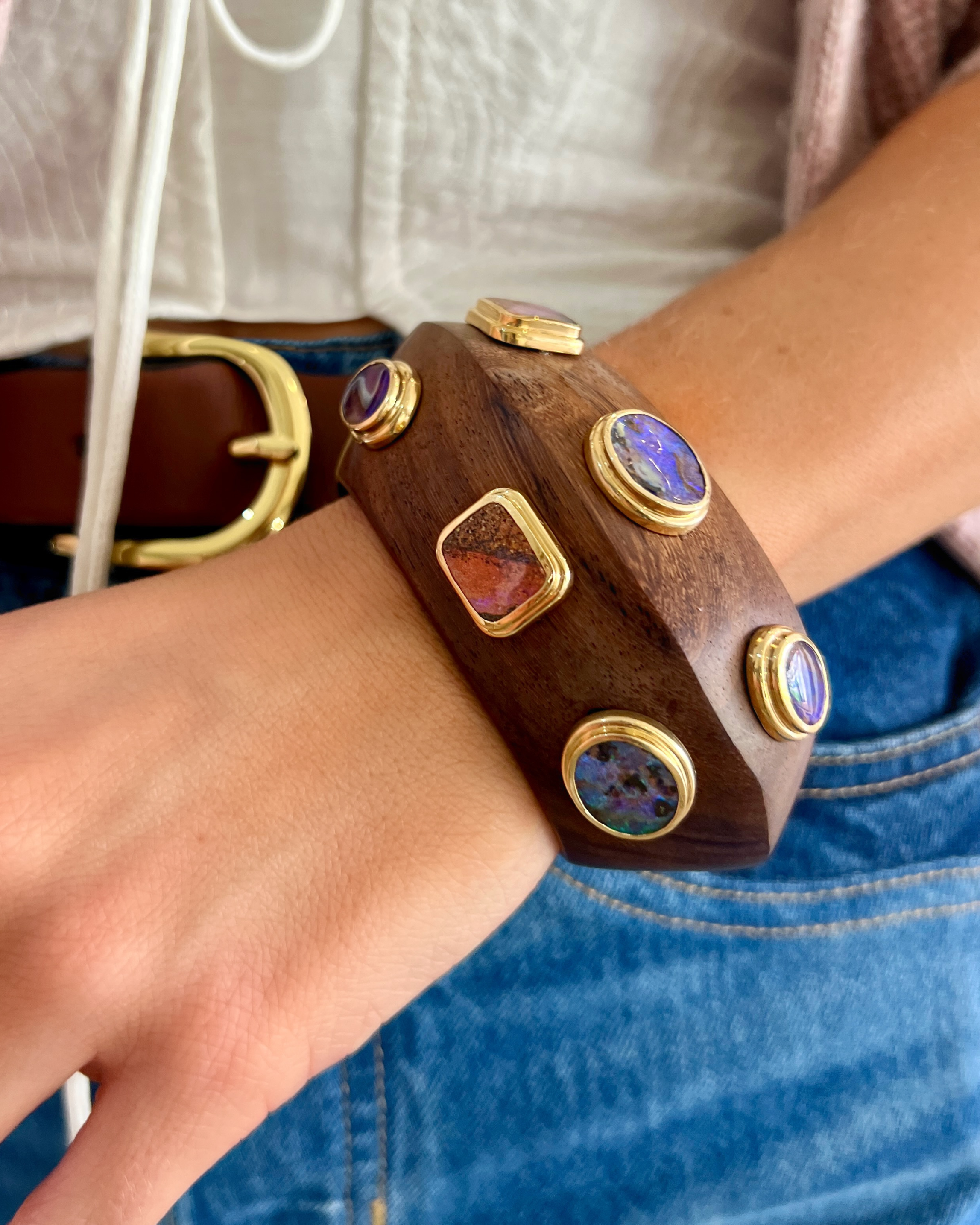 Brown leather bracelet with gemstone accents on a wrist, worn with blue jeans and a white shirt.