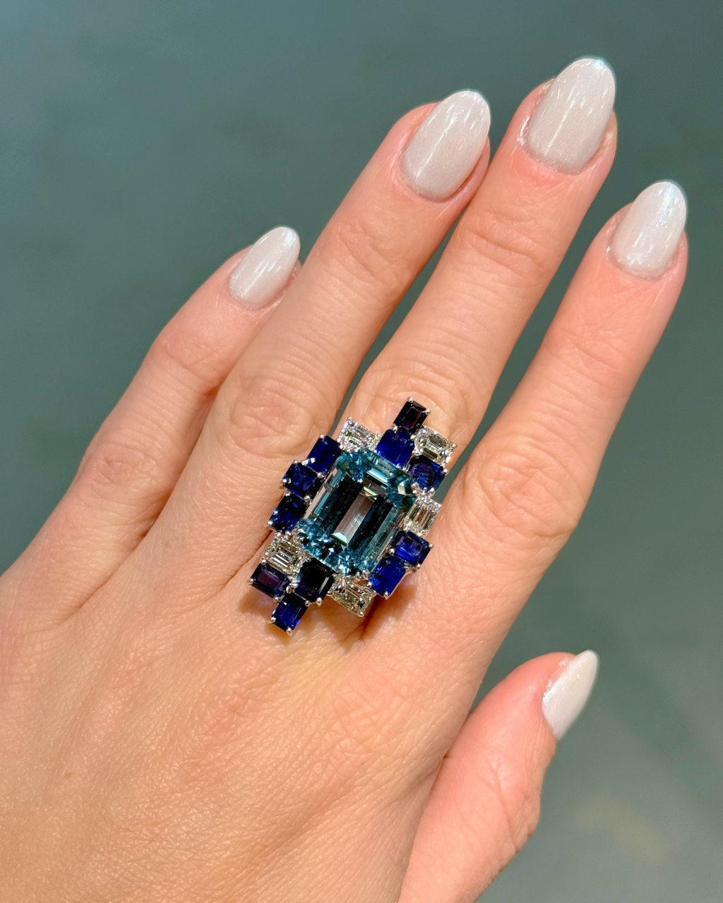 Hand wearing a ring with blue gemstones on a neutral background
