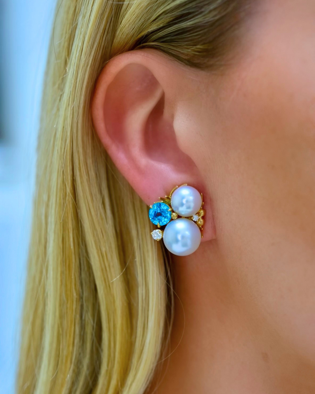 Close-up of an ear wearing a pearl and gemstone earring with blurred background