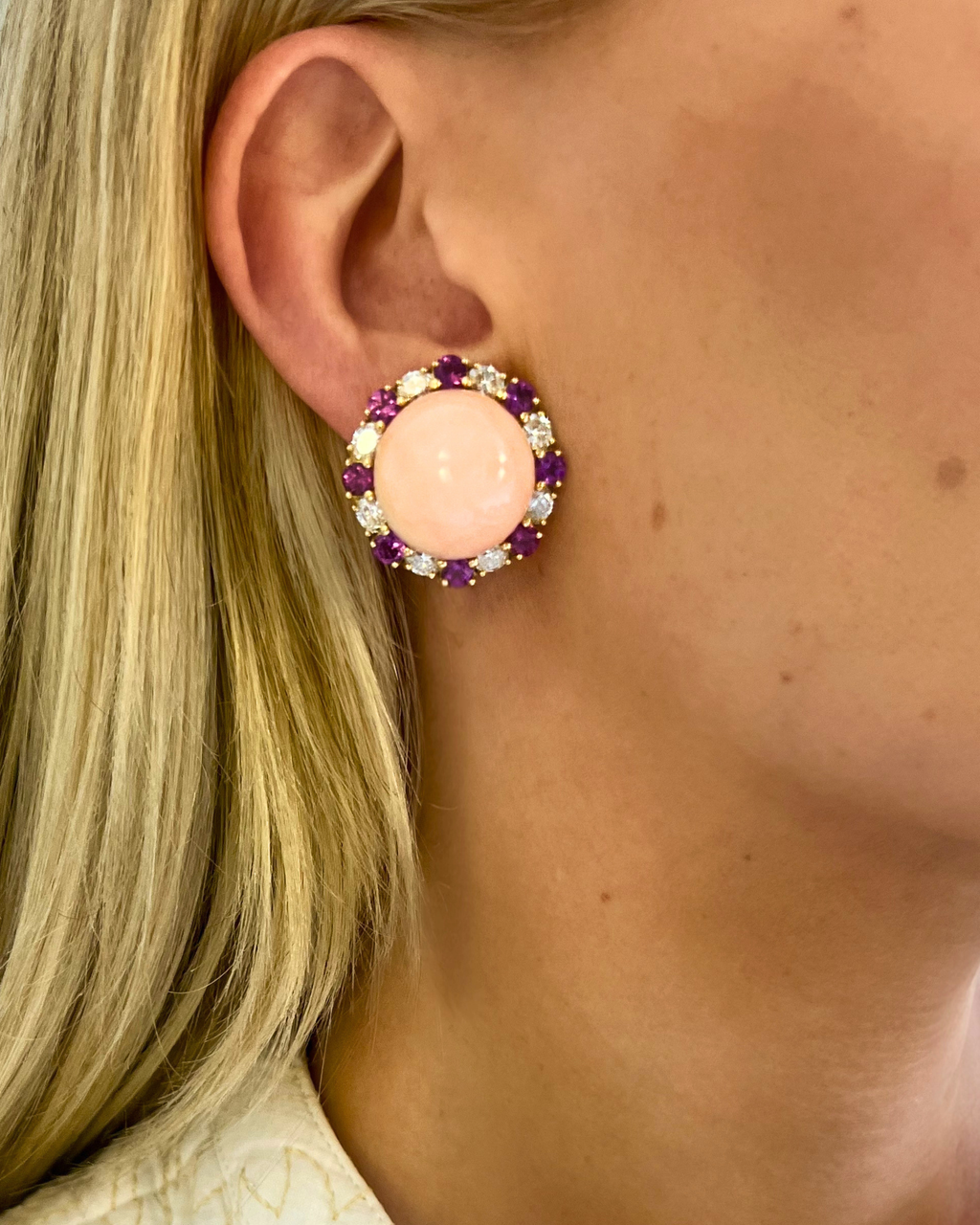Close-up of an ear wearing a pink earring with purple and gold accents.