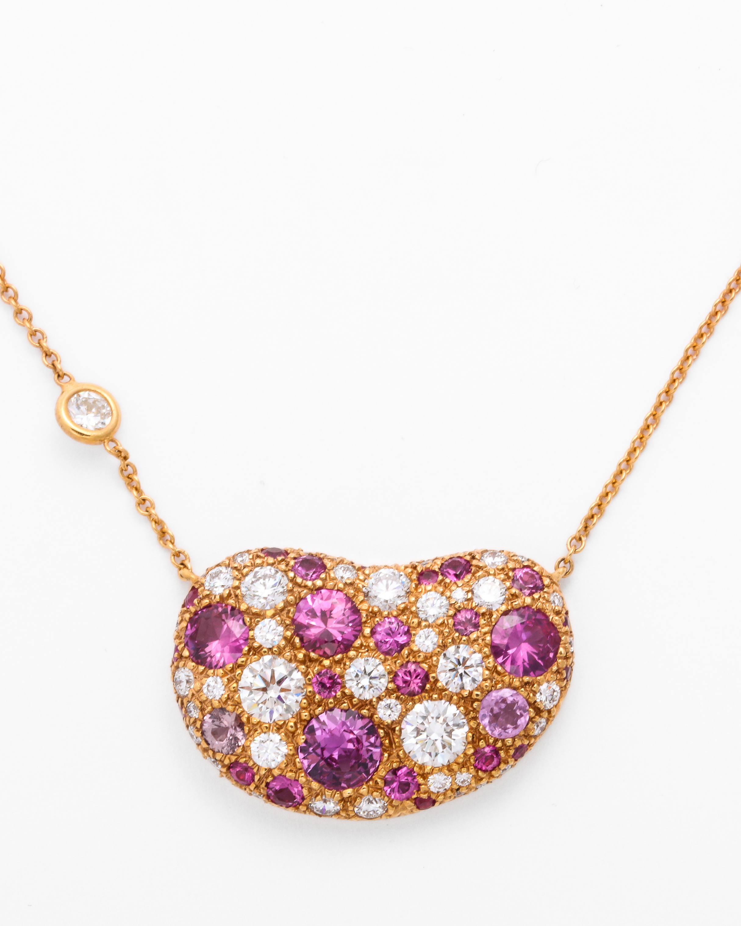 Gold necklace with a heart-shaped pendant featuring pink and white gemstones on a white background