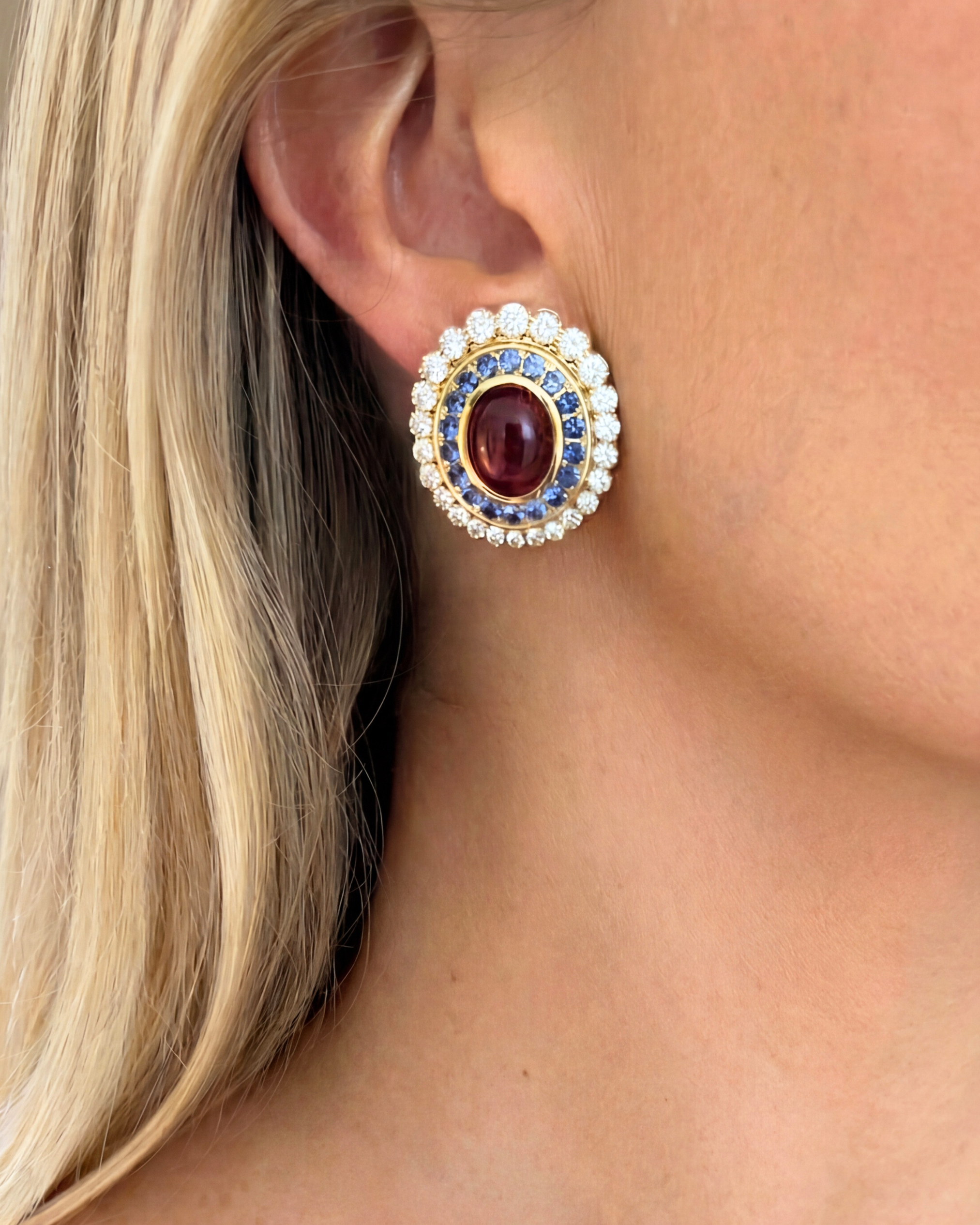 Close-up of a person wearing a decorative earring with a red gemstone and pearl accents.
