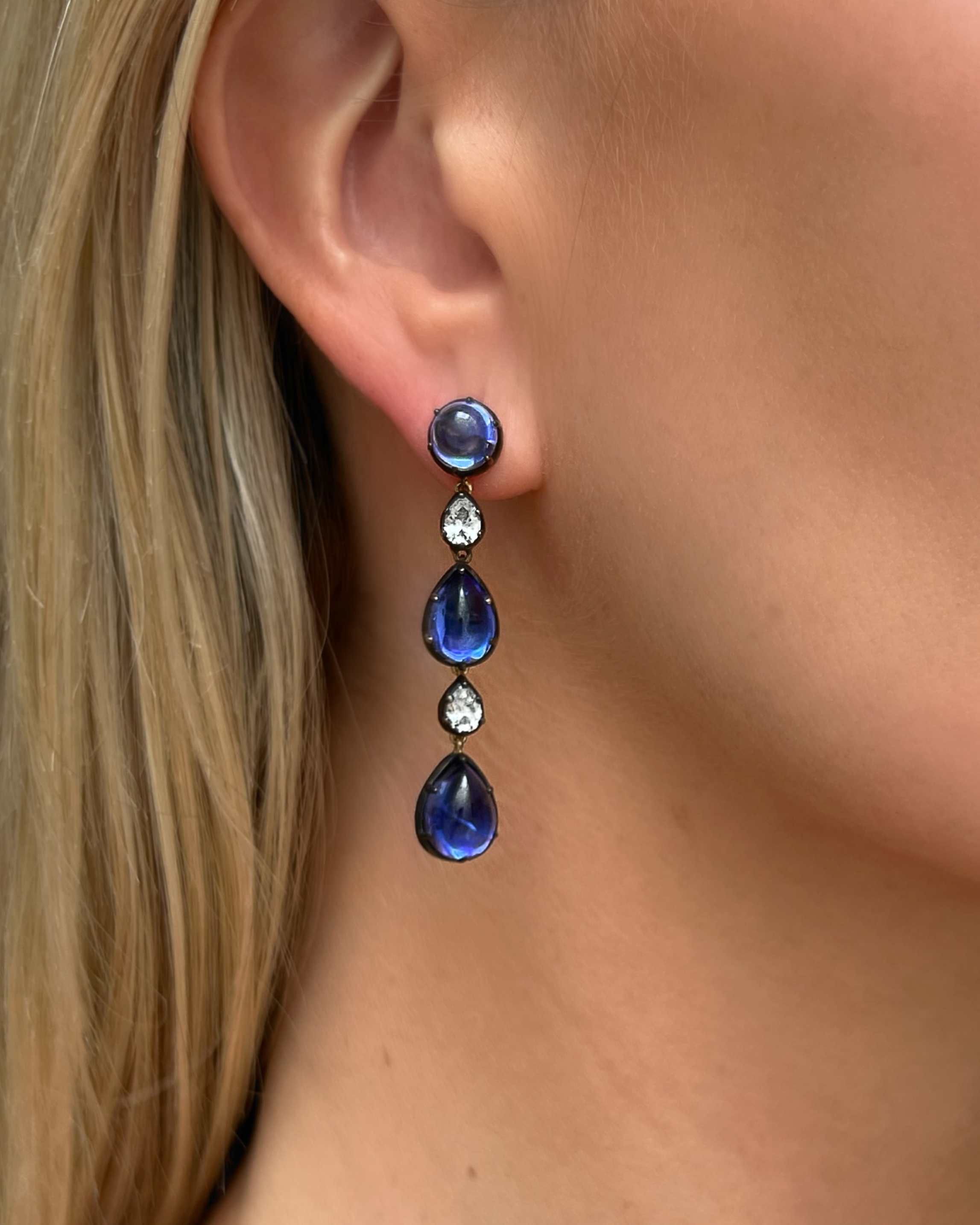 Close-up of a woman wearing blue teardrop earrings with a blurred background